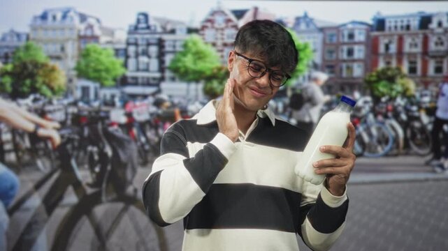 Man wearing glasses holding a milk bottle while rubbing his cheek for toothache on a busy urban street with parked bicycles; discomfort concern.