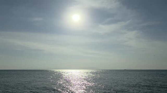 A serene ocean scene with the sun shining brightly in a blue sky with clouds