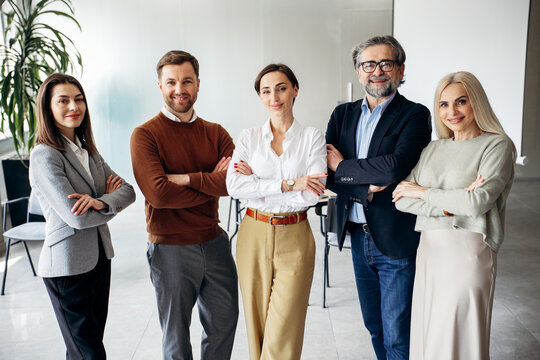 Group of confident professionals from different generations posing with crossed arms, representing teamwork and success