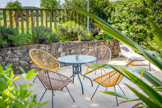 Un salon de jardin dans la nature, il y &agrave; 4 chaises autour d'une table au milieu de plantes, tout est sur une terrasse avec un muret 
