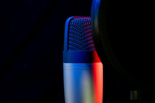 Professional studio microphone with a pop filter against a black background, illuminated by dramatic red and blue lighting
