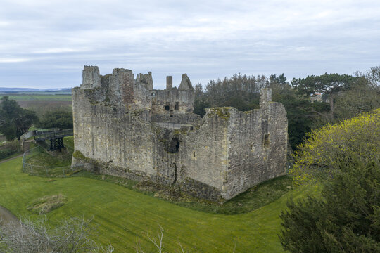 Aerial view of Dirleton Castle and Gardens featuring the historic ruined stone walls and lush green lawns under an overcast sky in Dirleton, Scotland, United Kingdom.