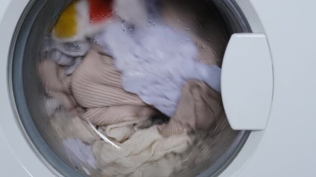 White washing machine cleaning laundry inside transparent drum. Process of washing clothes in modern appliance. Housework equipment for household textile cleaning.
