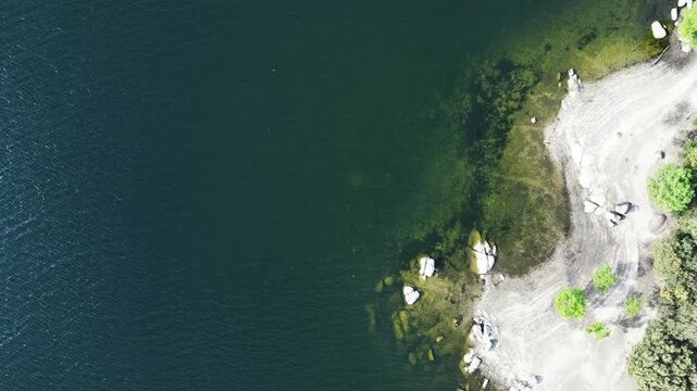 A rocky shoreline meeting emerald waters, with sparse greenery and clear patterns in the sand. Suitable for environmental studies or coastal geography projects.