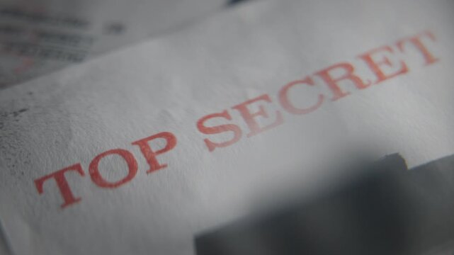 Top Secret red rubber stamp on government classified paper document retro old declassified information or censored sensitive text. Magnifying glass extreme close up. Grunge style. Confidential data