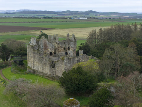 Aerial view of the historic stone ruins of Dirleton Castle and Gardens surrounded by lush green lawns and dense trees under an overcast sky in Dirleton, Scotland, United Kingdom.