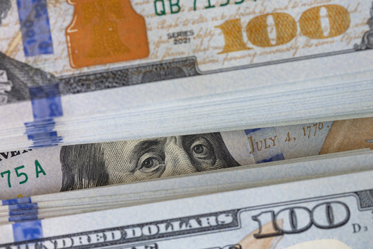 Macro view of US hundred dollar bills stack with Benjamin Franklin eyes peering through
