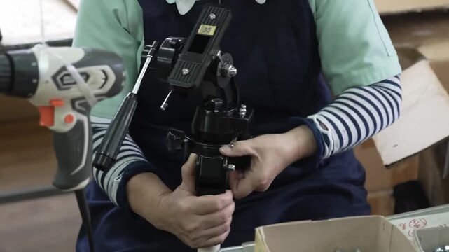 Factory worker holding assembled black equatorial mount head with cordless drill nearby for final tightening