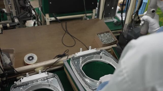 Assembly line worker installing screws into IH rice cooker inner frame housing with electric screwdriver