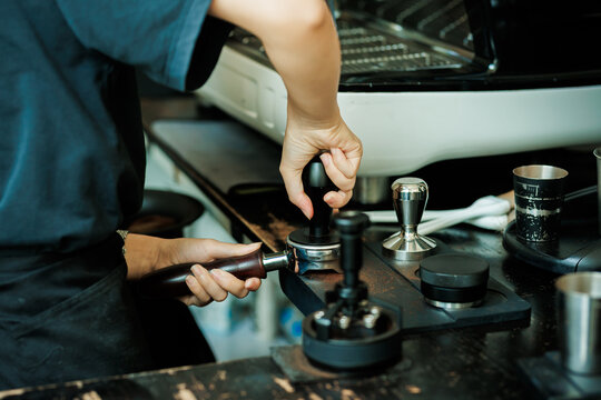 Close-up of a professional barista's hand using a metal tamper to press ground coffee in a portafilter.