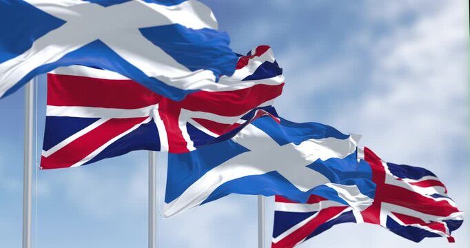 Scotland and UK flags waving in the wind on a clear day. White Saint Andrew cross on a blue background. Seamless 3d render animation. Slow motion loop. Selective focus