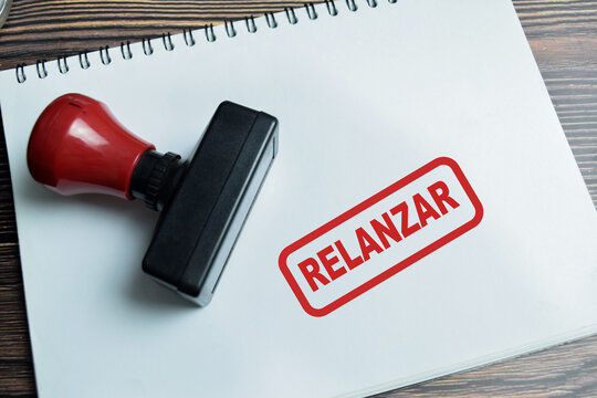 Red Handle Rubber Stamper and Relanzar in Spanish it means Relaunch text above book isolated on wooden background
