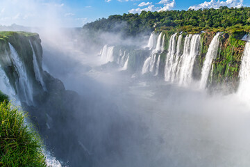 Fototapeta premium Panoramic scenic view of Iguazu Falls with mist and lush green tropical forest on a sunny day, Misiones Province, Argentina