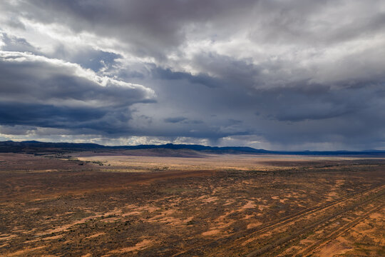 Aerial view of the vast arid outback landscape with red soil and sparse vegetation under dramatic storm clouds in Flinders Ranges, South Australia, Australia.