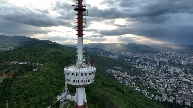 Aerial shot of the iconic Tbilisi TV Broadcasting Tower on Mtatsminda Mountain overlooking the city architecture during daytime.