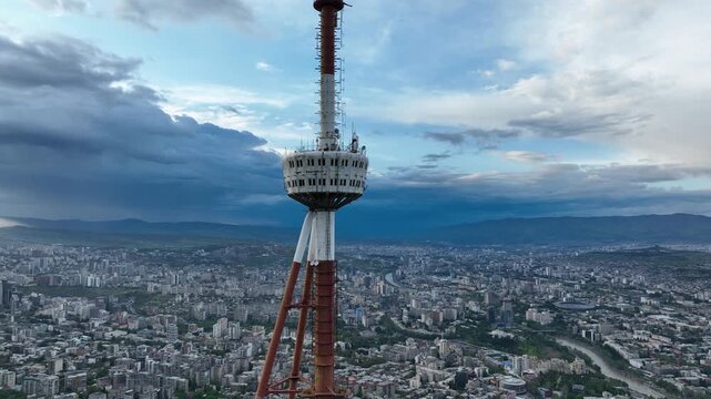 Aerial shot of the iconic Tbilisi TV Broadcasting Tower on Mtatsminda Mountain overlooking the city architecture during daytime.