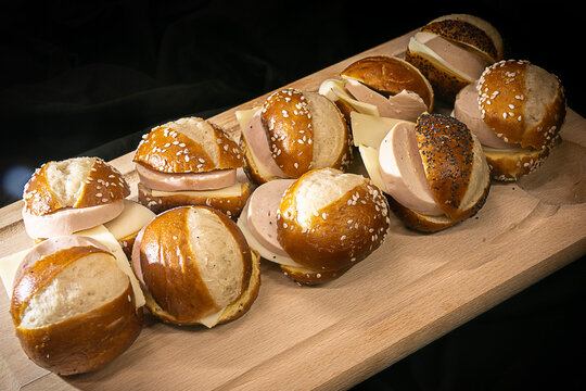 Assorted mini pretzel bun sandwiches with ham and cheese on a wooden board