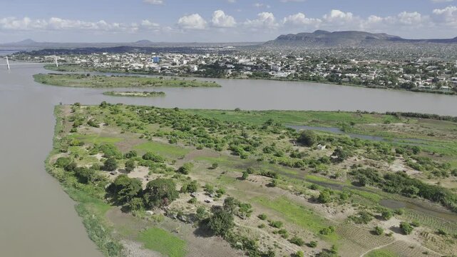 Drone orbits right over island on Zambezi River with ultra wide view of Samora Machel Bridge on a sunny day in Tete, Mozambique