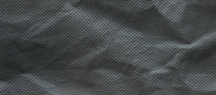Crumpled black non-woven fabric texture, wrinkled dark synthetic material background, industrial charcoal textile surface with micro-perforations