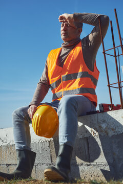 Construction worker having a heatstroke on a hot sunny day, headache, issues on a construction site outdoors.