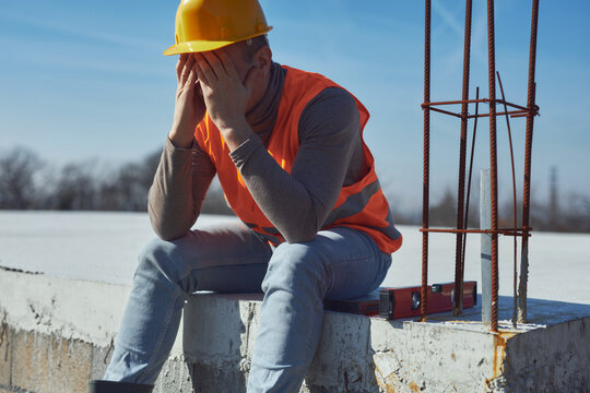Construction worker having a heatstroke on a hot sunny day, headache, issues on a construction site outdoors.
