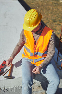 Construction worker working outdoors on a construction site, making a pause and holding a yellow hardhat.