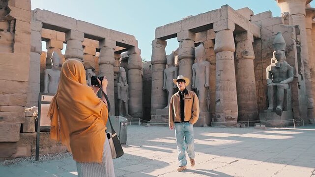 beautiful tourist holding a camera taking pictures of ramsses statue and her family in luxor temple, Luxor, Egypt.