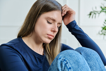 Unhappy upset young woman sitting on chair at home