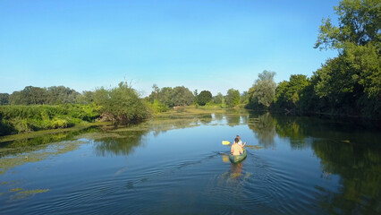 Obraz premium AERIAL: Active young couple paddles their canoe down a tranquil dark blue river.