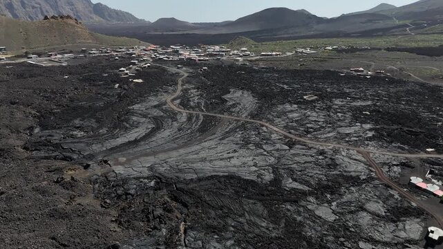 Aerial view of the remote village of Ch&atilde; das Caldeiras built directly upon the vast black solidified lava fields of Fogo Volcano in Cabo Verde, surrounded by towering volcanic crater walls