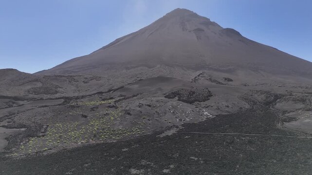 Wide aerial shot showing the majestic conical shape of Pico do Fogo, Cabo Verde, rising dramatically from the dark, expansive volcanic plains of the surrounding caldera