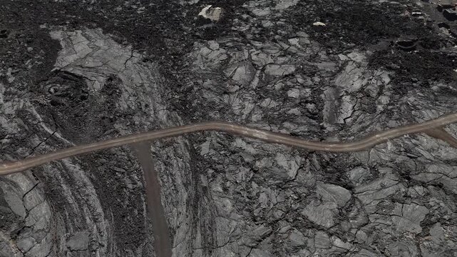 top down drone view of the black solidified lava fields and winding dirt paths at the base of Fogo Volcano, Cabo Verde, emphasizing the stark, desolate contrast of the volcanic landscape