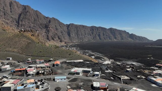 Aerial perspective of the Ch&atilde; das Caldeiras settlement at the base of the Bordeira mountain, local houses built on the dark volcanic terrain and lava fields of Fogo Island, Cabo Verde