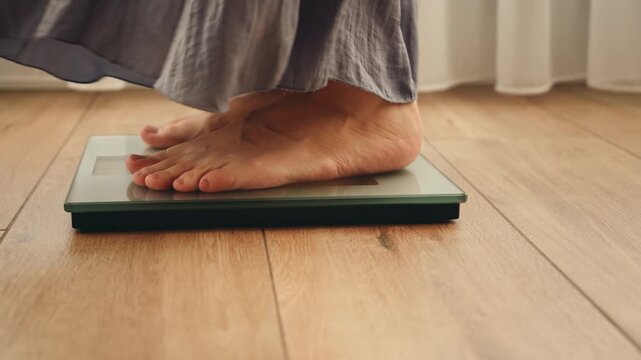 Close up person legs bare feet stepping onto weighing scale at home room. Fitness diet BMI girl slimming healthy lifestyle weight awareness concept. Woman weight lose standing on scales measure weight
