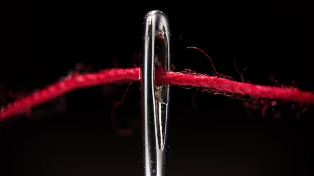 Red thread passing through eye of a needle sewing macro