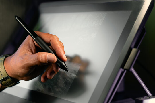 Close-up of left-handed digital artist drawing on graphic tablet with stylus pen in modern creative workspace