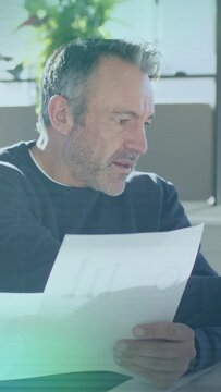 Vertical video: Man picking finance paper on sofa reading charts checking sums while light crossing