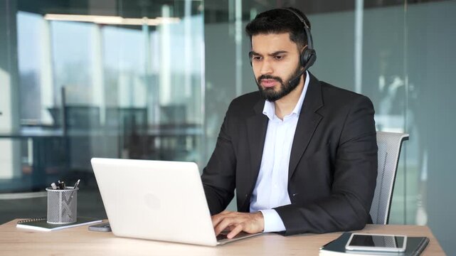 Male corporate operator in headset and suit working in customer support service on helpline telesale talking using laptop in business office. Agent of call center advises client by answering questions