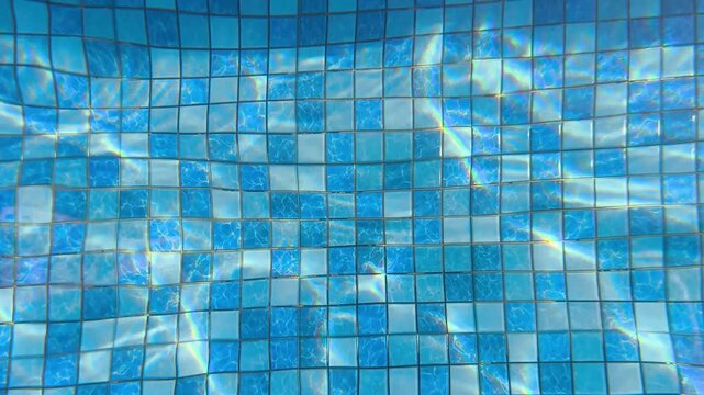 Close-up of a swimming pool's blue mosaic tile surface with rippling water reflections.