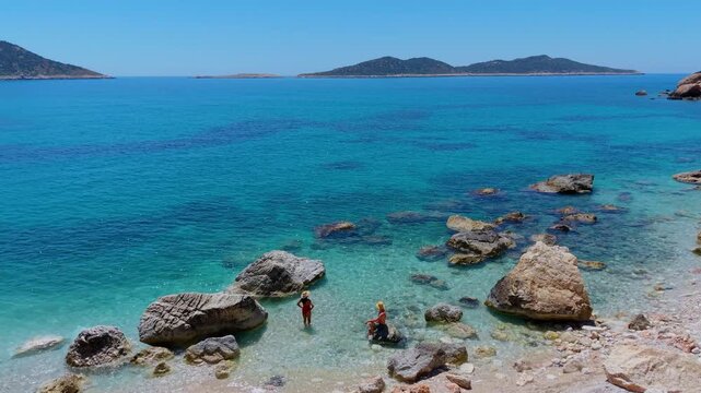 Visitors explore the tranquil beaches of Kas, Turkey, surrounded by stunning rock formations and vibrant blue waters.