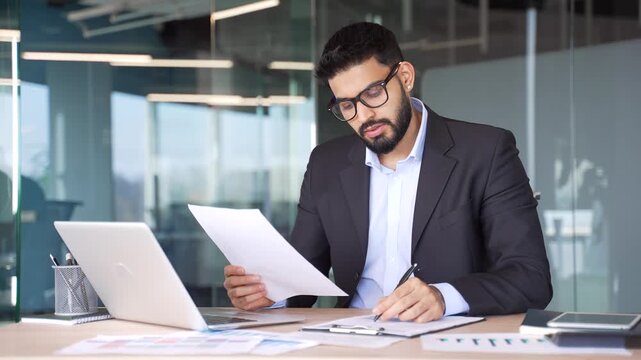 Busy businessman in formal suit is doing paperwork sitting at desk at workplace in business office. Financier working fills out documents, writing takes notes, making tax return, engaged in accounting