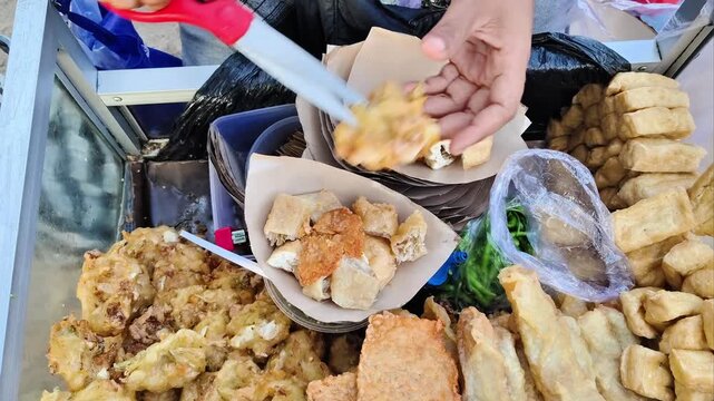 Indonesian street food vendor cutting fried snacks (lumpia) into paper wrap. 