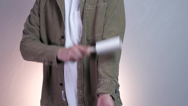 Young man using a lint roller to remove pet hair and fluff from his sleeve. Daily wardrobe maintenance before leaving home. Perfect for pet care, hygiene, and fashion lifestyle videos. Crisp and clean