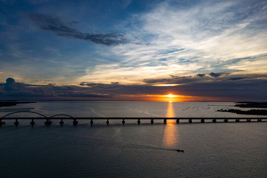 Aerial view of Bintan Island with a long arched bridge spanning the sea during a vibrant sunset with golden light reflecting on the water Tanjung Pinang, Riau Islands, Indonesia.