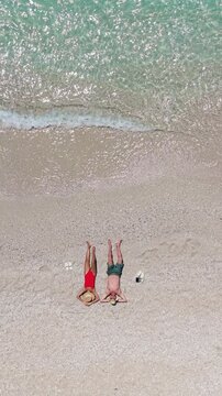 Friends relax on a vibrant beach in Kas, Turkey, flipping upside down in joy. Crystal-clear waters sparkle under the sun, creating a perfect setting for holiday fun and laughter. drone top view