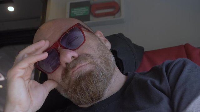 Vertical: Bald man with a red goatee sits thoughtfully on a train seat, reflecting quietly during a calm and contemplative journey.
