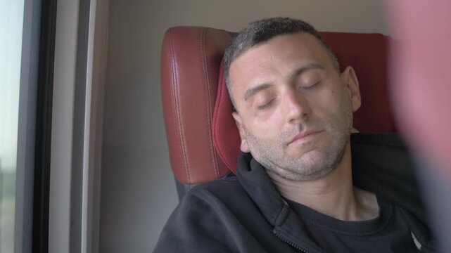Young dark-haired man sleeping comfortably in a first class train seat during a peaceful daytime journey.