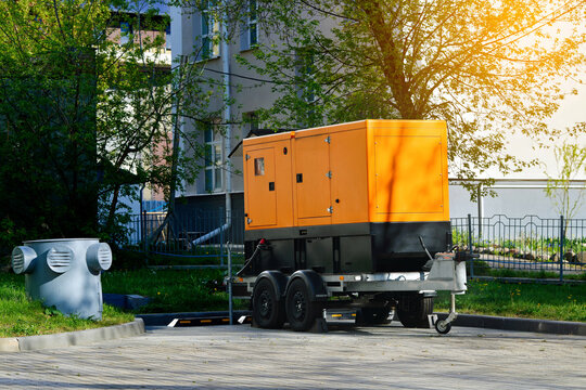 Mobile diesel generator on trailer in city parking lot. Portable industrial power station for emergency backup energy. Backup generator providing temporary electricity supply near residential building