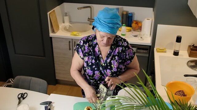 Elderly woman in kitchen grating apple for homemade pie. Footage showing cooking process and ingredient preparation.