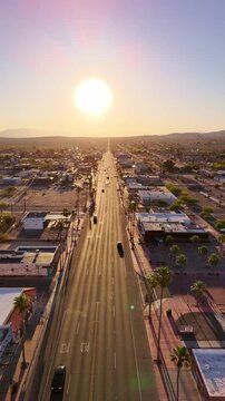 An aerial drone shot looking down the long straight expanse of Twentynine Palms Highway into a bright rising sun casting long shadows over the desert town of Twentynine Palms, California, USA.